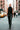 Person in black outfit walking on a city street with taxis and pedestrians in the background
