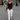 Woman walking on a city street wearing a black top and white pants.