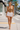 Woman walkng down the street on vction wearing a backless fringe to with white denim shorts.